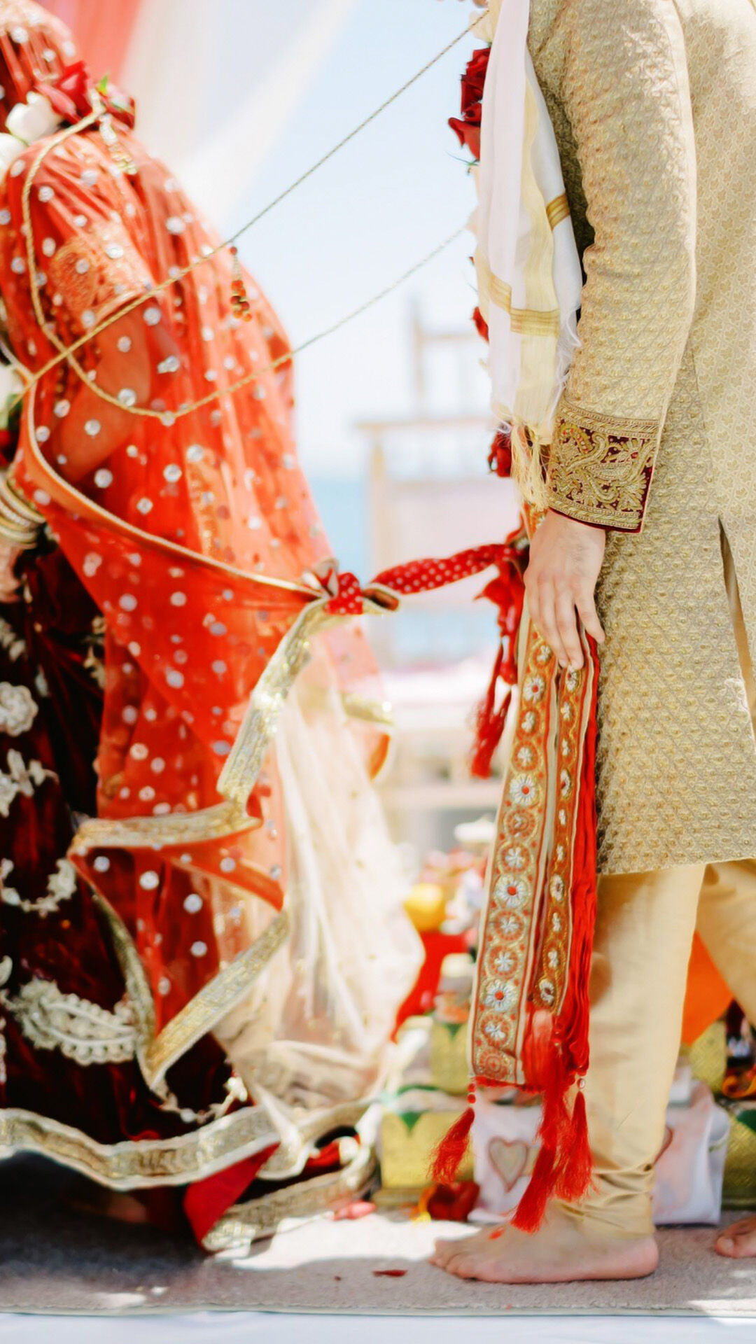 Indian bride and groom in traditional wedding attire holding hands during Saptapadi ritual with red and gold outfits and kalire